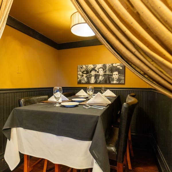 A cozy Italian restaurant dining nook with a set table, black and gold walls, and a framed picture.