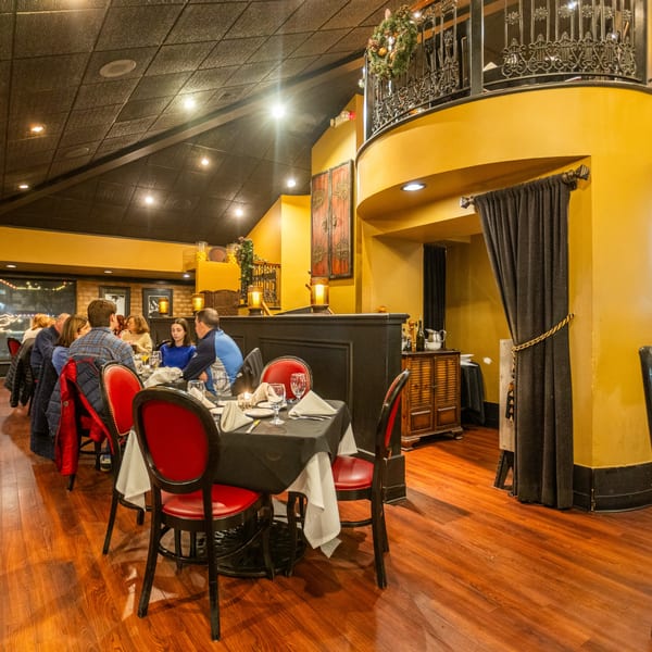 Diners seated at tables with red chairs in the Sapore Italian Cafe, featuring a balcony and warm lighting.