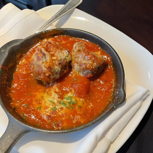 Two large meatballs in rich red marinara sauce with melted cheese and herbs in a cast iron pan.