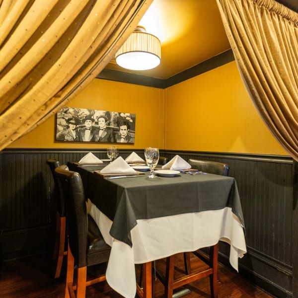 A private dining nook at Sapore Italian Cafe with a set table, yellow walls, and a vintage painting.