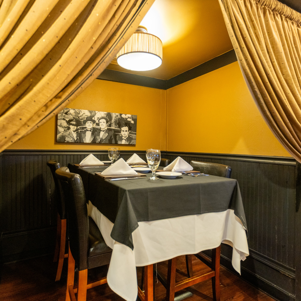 A private dining nook at Sapore Italian Cafe with a set table, yellow walls, and a vintage painting.