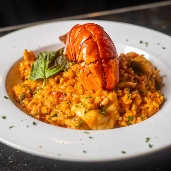 A vibrant orange lobster tail and fresh basil garnish a rich seafood risotto on a white plate.