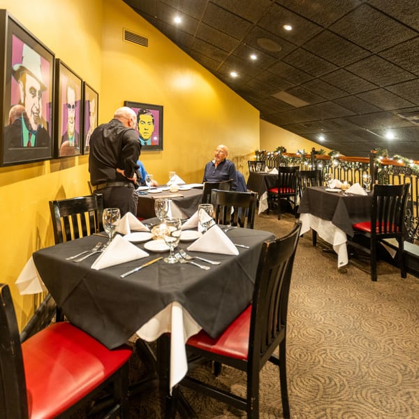 Sapore Italian Cafe's dining room with yellow walls, pop art, set tables, and a server assisting a guest.