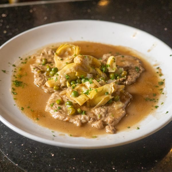Veal scallopini with artichokes, peas, and parsley in a light brown sauce on a white plate.