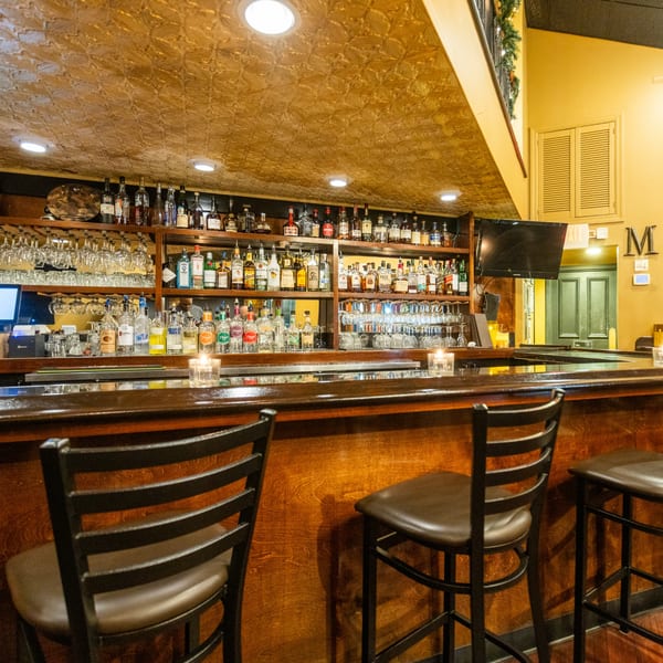 A well-stocked bar at Sapore Italian Cafe with bottles, glasses, and bar stools.